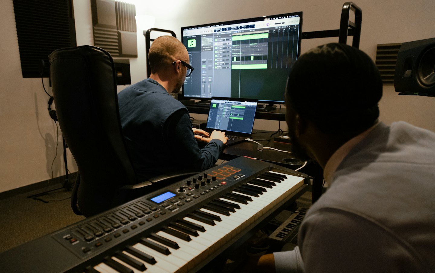 Dos hombres trabajando juntos en un estudio de música con un teclado MIDI.